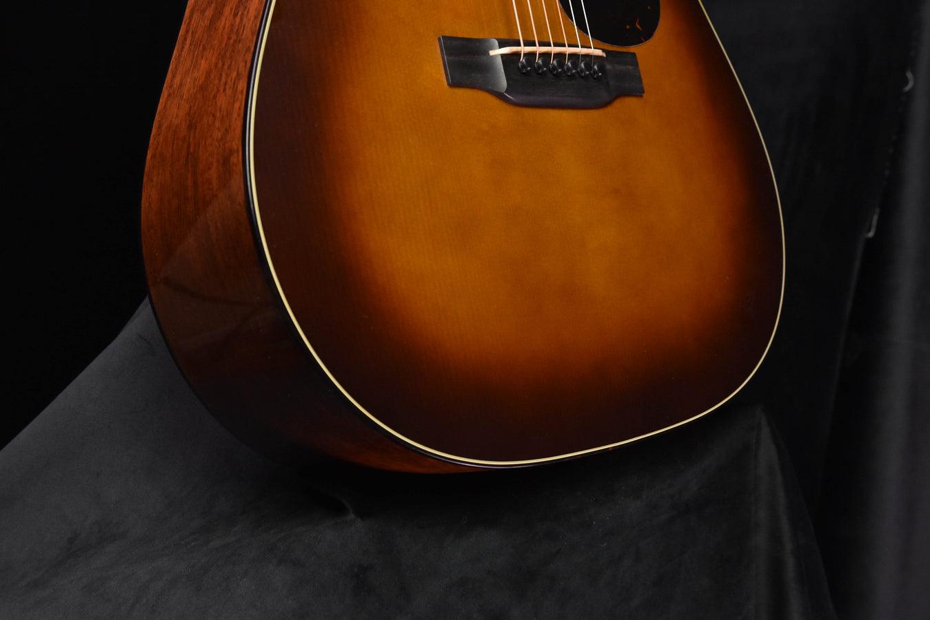 Amber burst acoustic guitar body close-up, showing lower bout and pickguard area