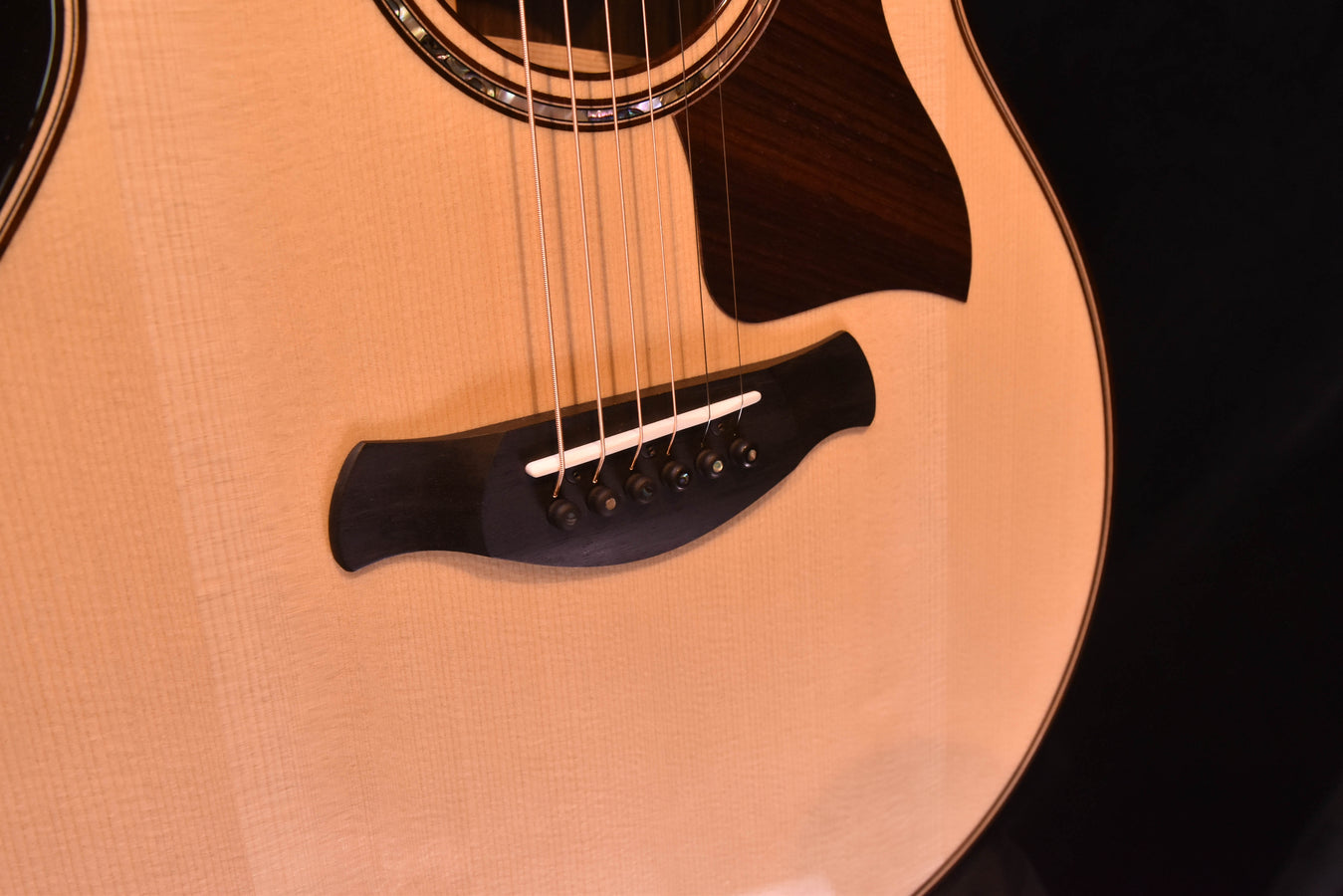 Guitar bridge and strings on a light wood top with dark pickguard