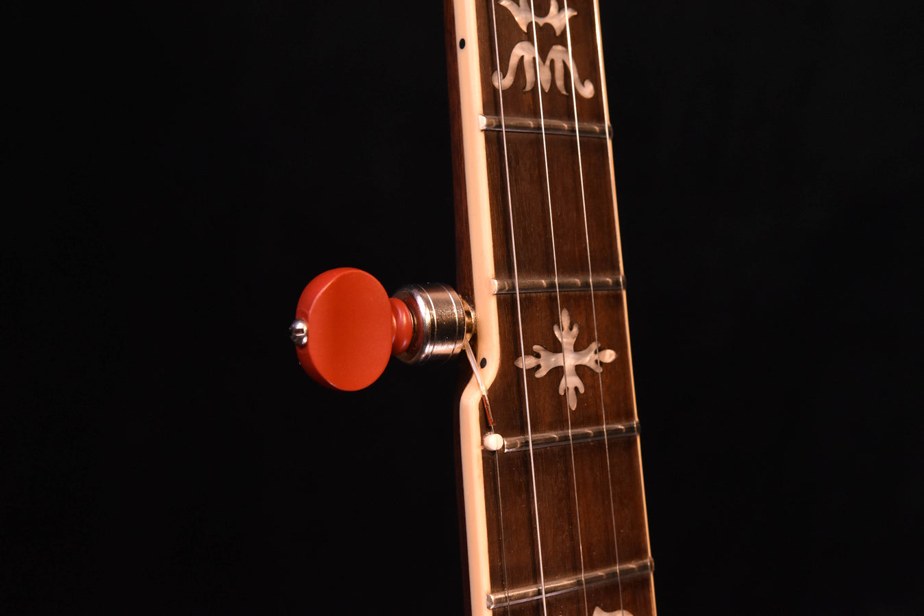 Banjo tuner close-up with red knob and engraved cross-style fretboard inlay