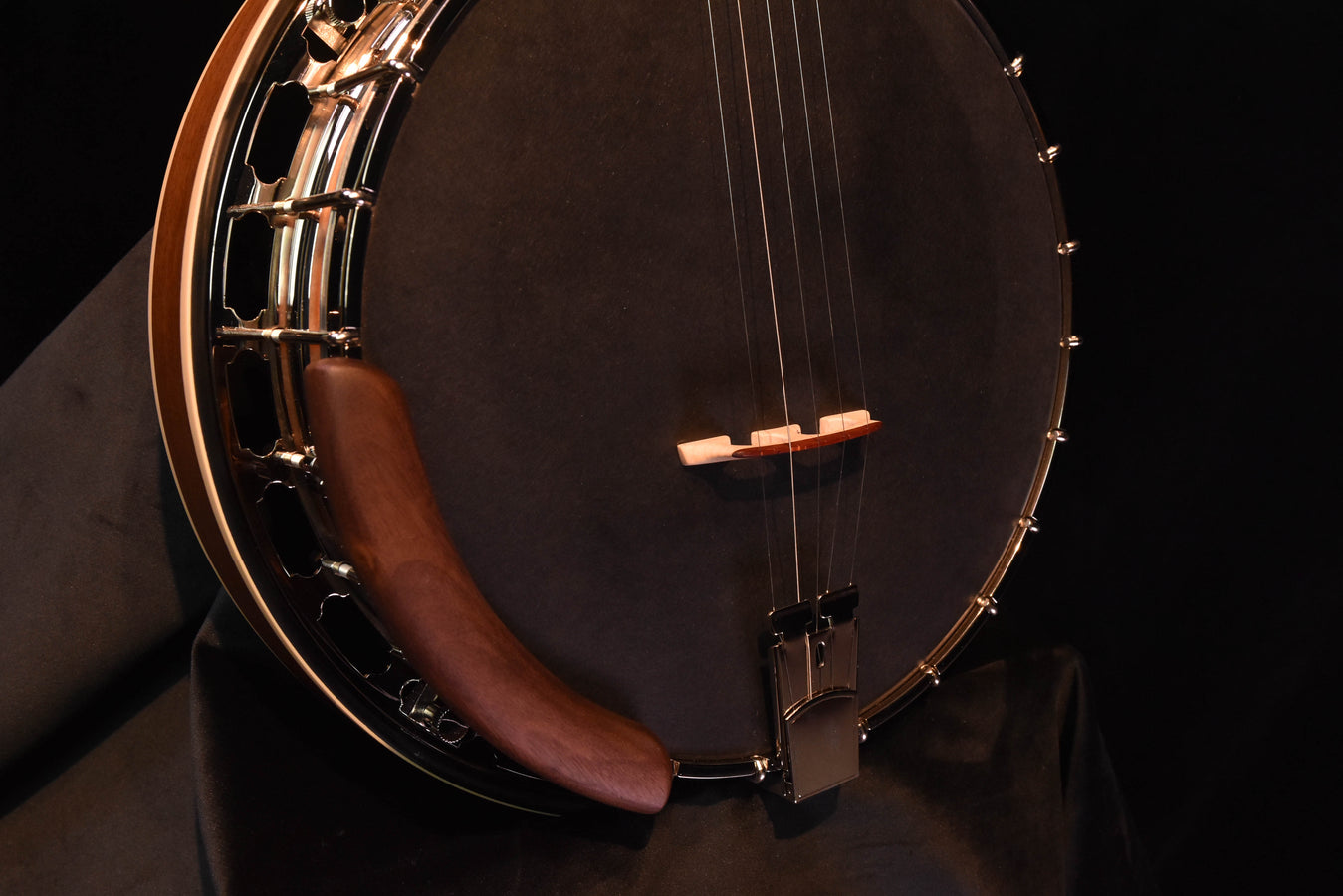 Banjo body close-up with dark drumhead, wooden bridge, and tailpiece hardware