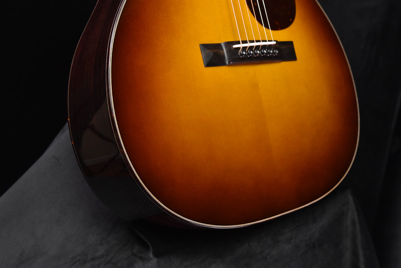 Sunburst OM acoustic guitar lower bout with bridge area and white binding