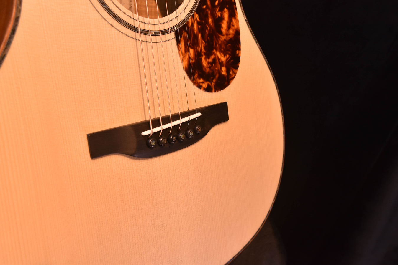 Acoustic guitar lower bout close-up with black pickguard and visible bridge saddle