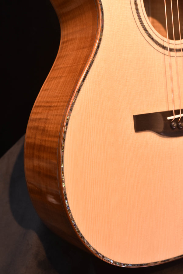 Acoustic guitar side close-up showing curved body, binding and warm brown finish