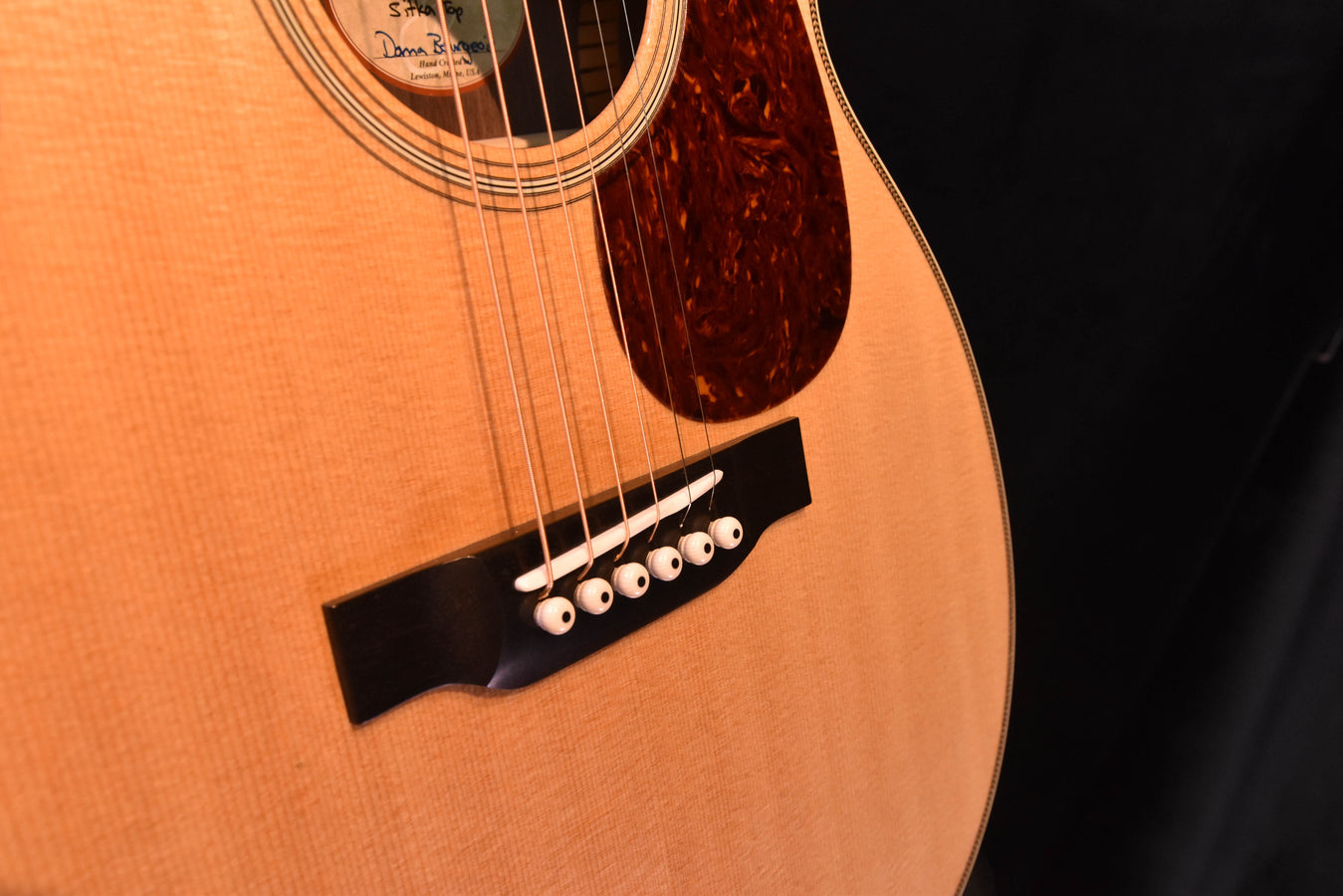 Acoustic guitar bridge and strings close-up on light top with dark pickguard