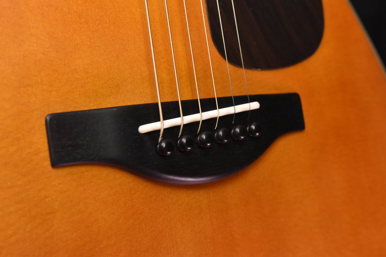 Black bridge with adjustable saddle and six strings on acoustic-electric guitar top
