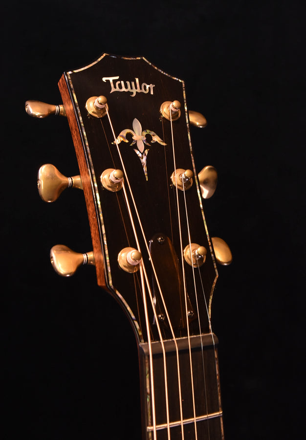 Taylor guitar headstock with inlaid logo and gold tuning pegs on dark wood background