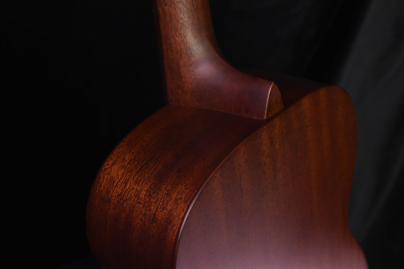 Used acoustic guitar side view of upper bout and neck, dark wood finish