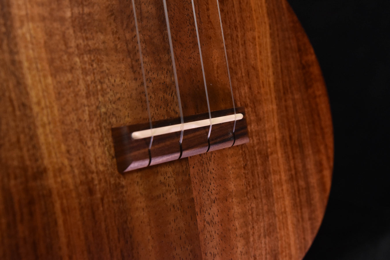 All-Koa concert ukulele, close-up of bridge and strings on the soundboard