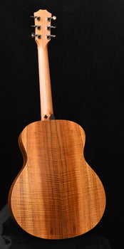 figured koa acoustic guitar body with slotted bridge and four tuning pegs