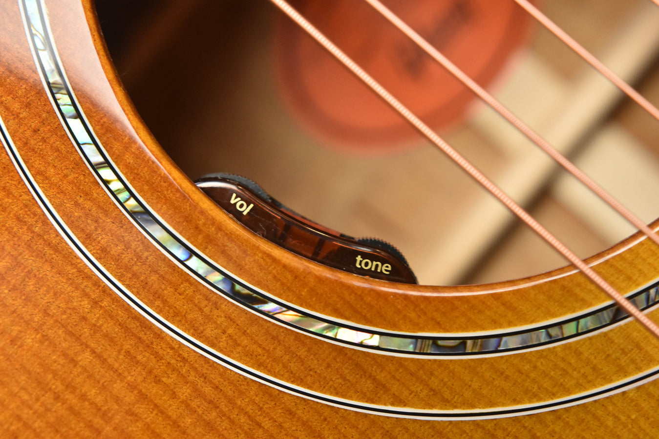 Acoustic guitar side view showing “vol” and “tone” control knobs near soundhole edge