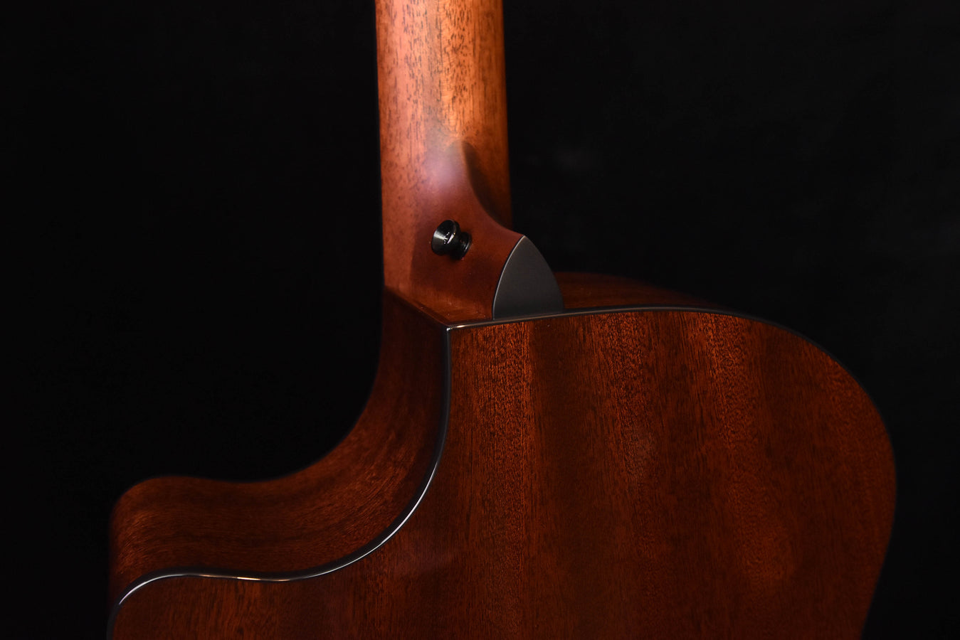 Side view of warm brown guitar body with neck joint and cream-colored binding