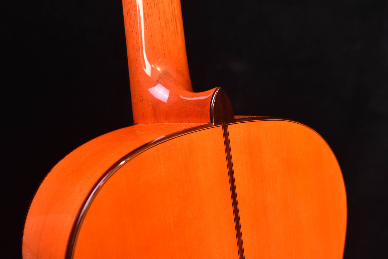 Upper bout and neck joint of orange flamenco guitar, glossy wood grain