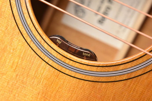acoustic-electric guitar bridge area with “vol” and “tone” controls under strings