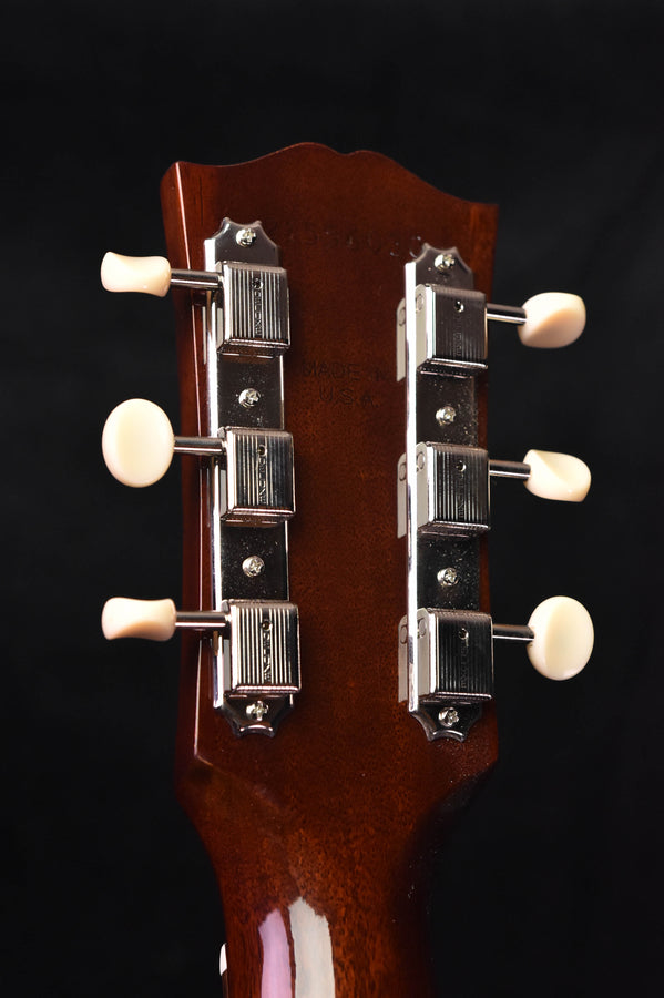 Acoustic guitar headstock with tuning machines on a dark brown wood panel