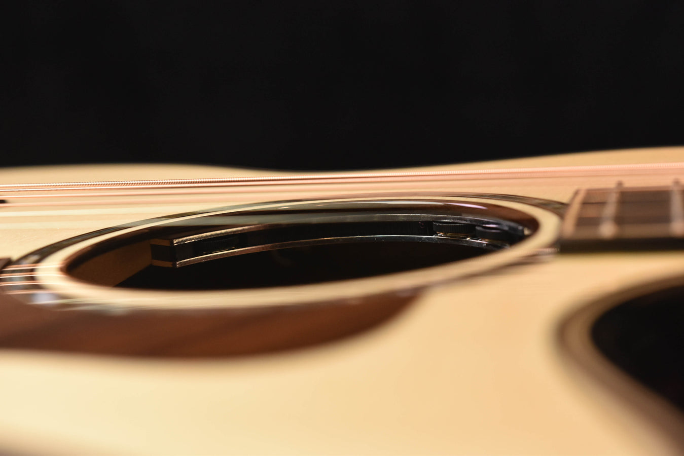 Acoustic guitar soundhole area with dark rosette and strings near the neck.