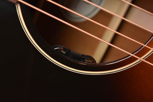 close-up of acoustic guitar strings over volume and tone knobs