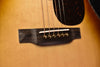 Acoustic guitar bridge area with dark pickguard and gold string pins