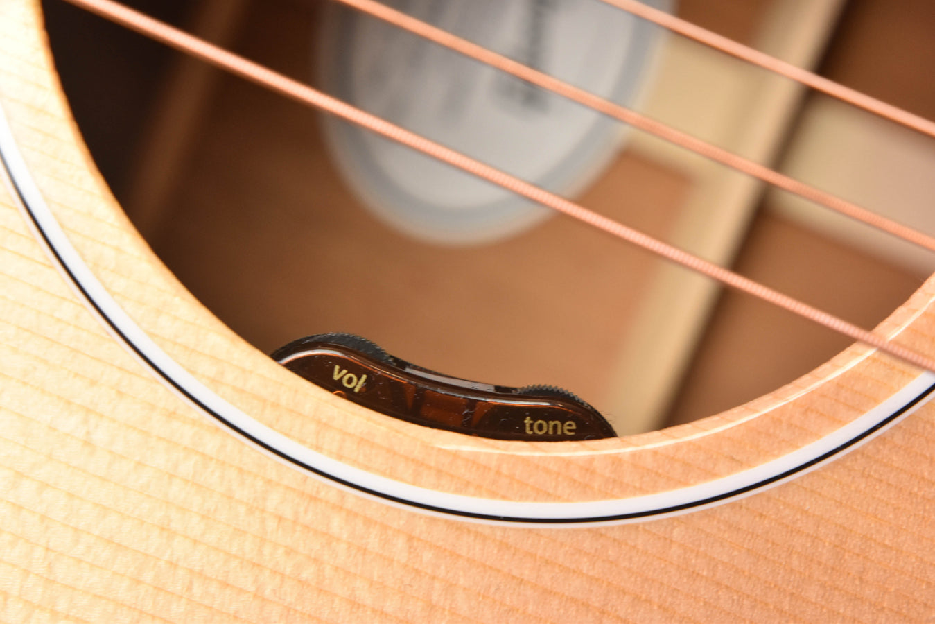 Guitar soundhole control labels showing 'vol' and 'tone' on light wood