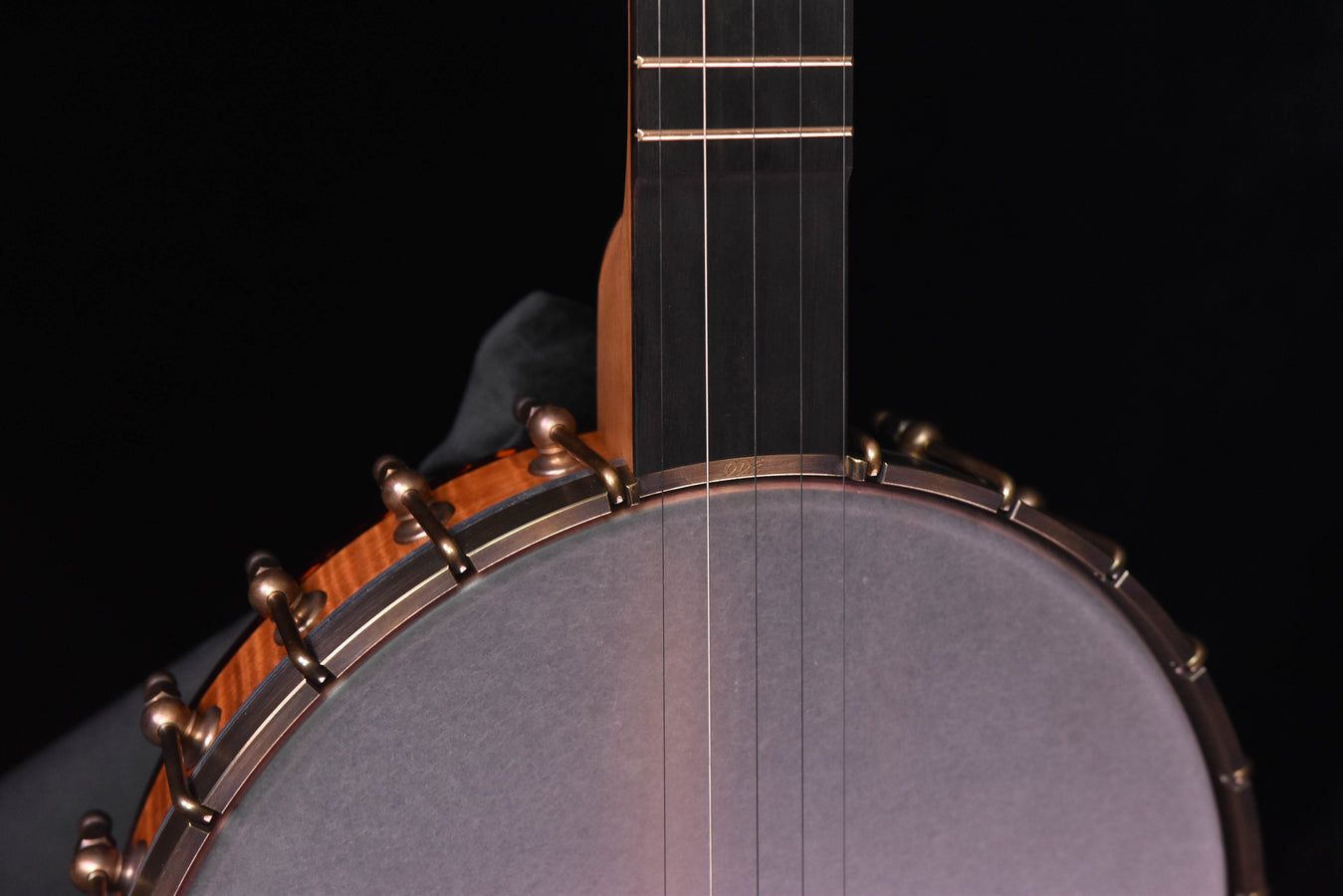 Banjo neck and strings above grey resonator head with wooden rim