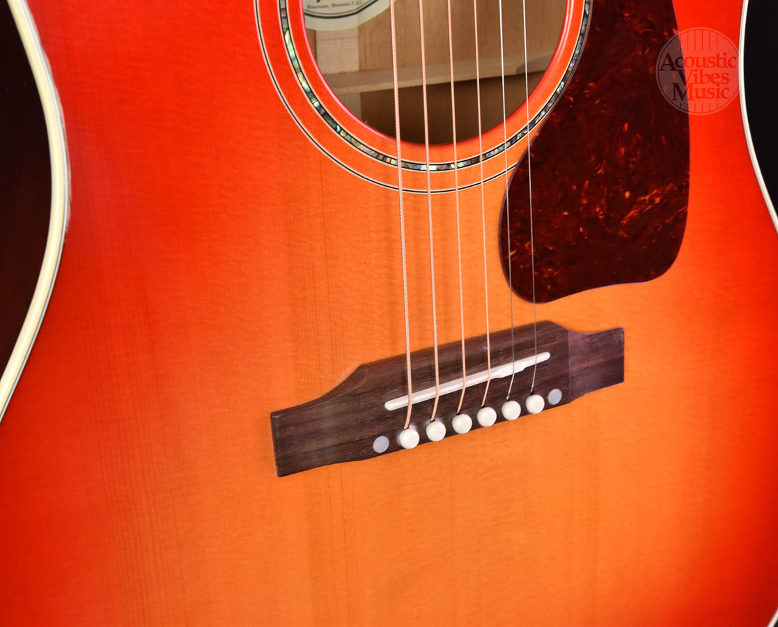 Close-up of cherry burst acoustic guitar bridge, strings, and pickguard area