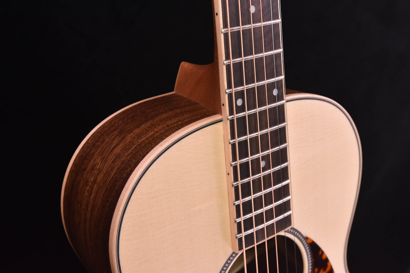 Parlor guitar close-up: curved dark wooden side and neck with fretboard and inlays
