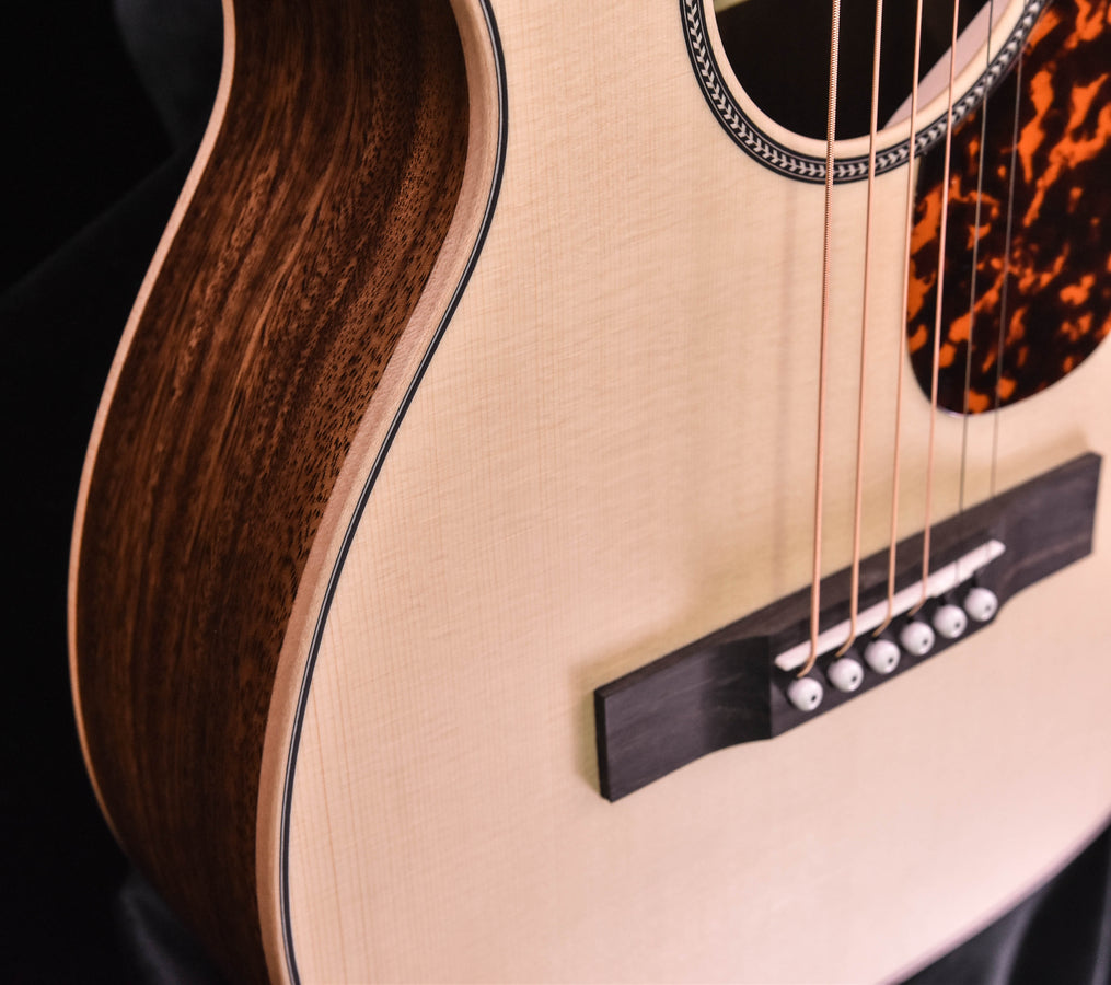 Acoustic guitar soundboard detail with dark bridge, strings, and tortoise-style pickguard edge