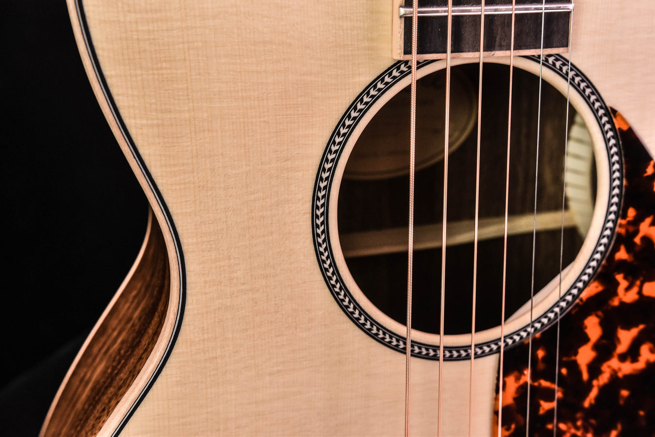 Sound hole close-up with patterned rosette and visible strings over pale spruce top