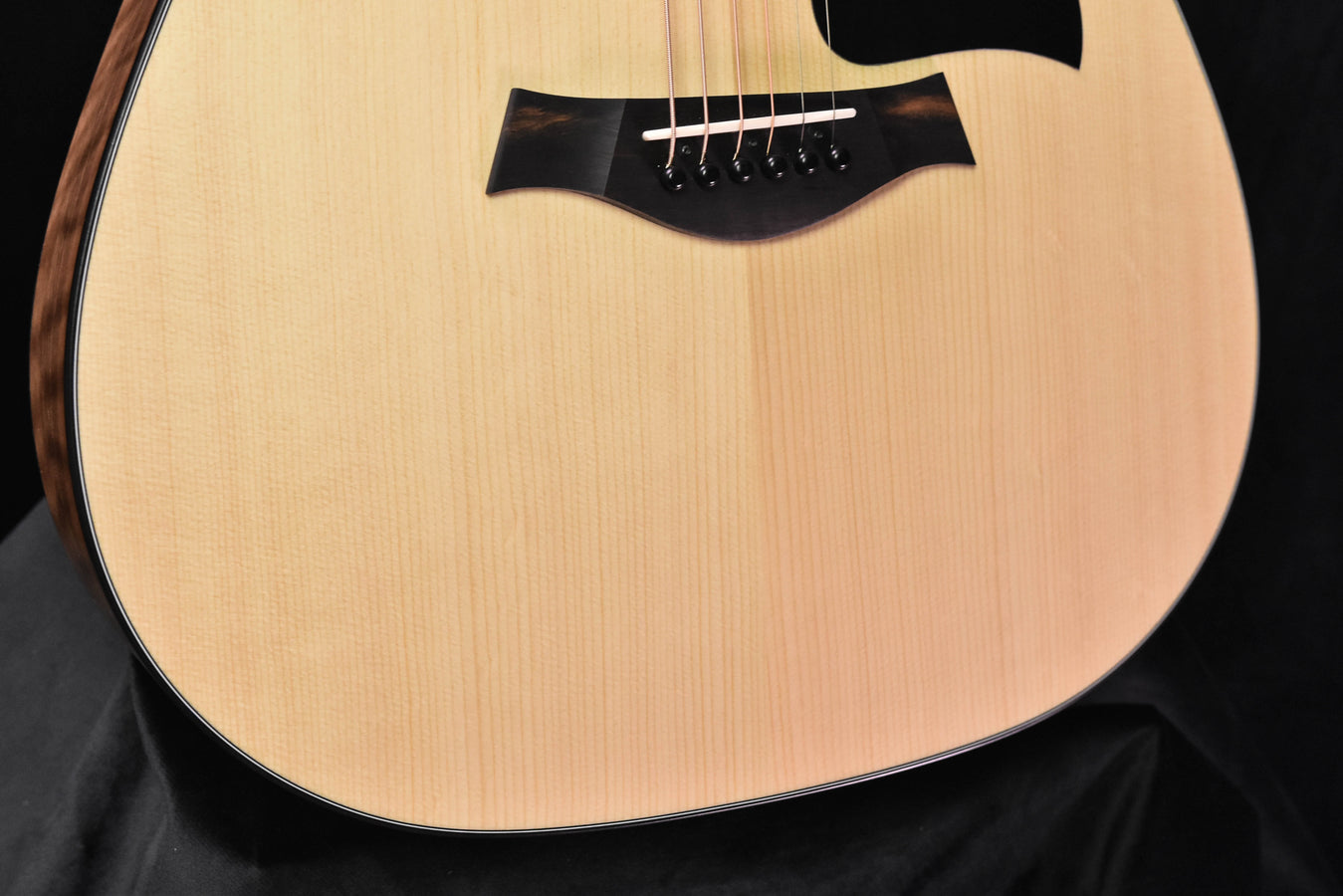 Natural acoustic guitar body close-up with black pickguard and bridge area