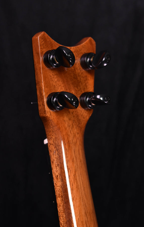 Tenor ukulele headstock close-up with four black tuning pegs on koa wood
