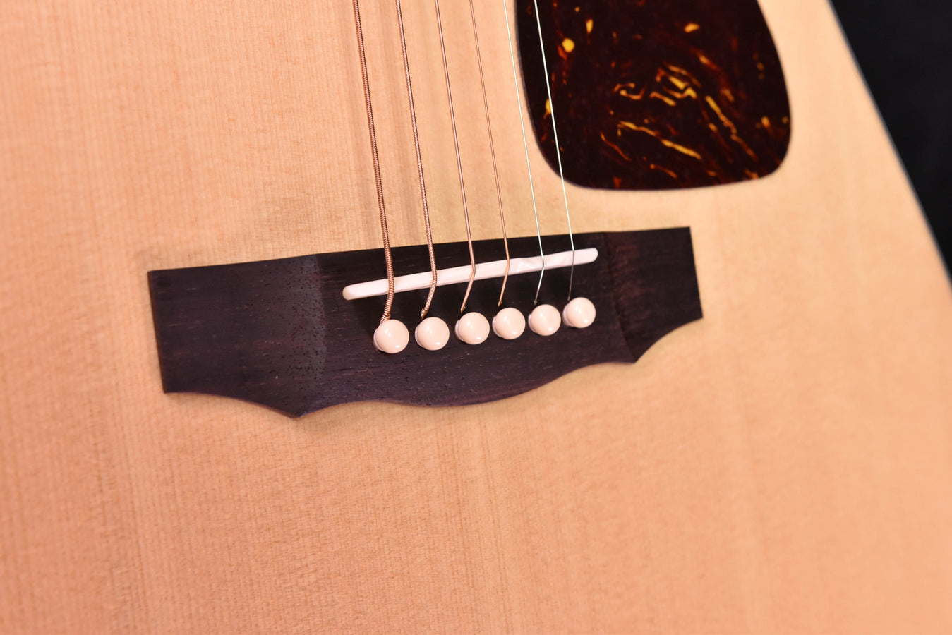 Close-up of natural-finish acoustic guitar bridge area and six white bridge pins