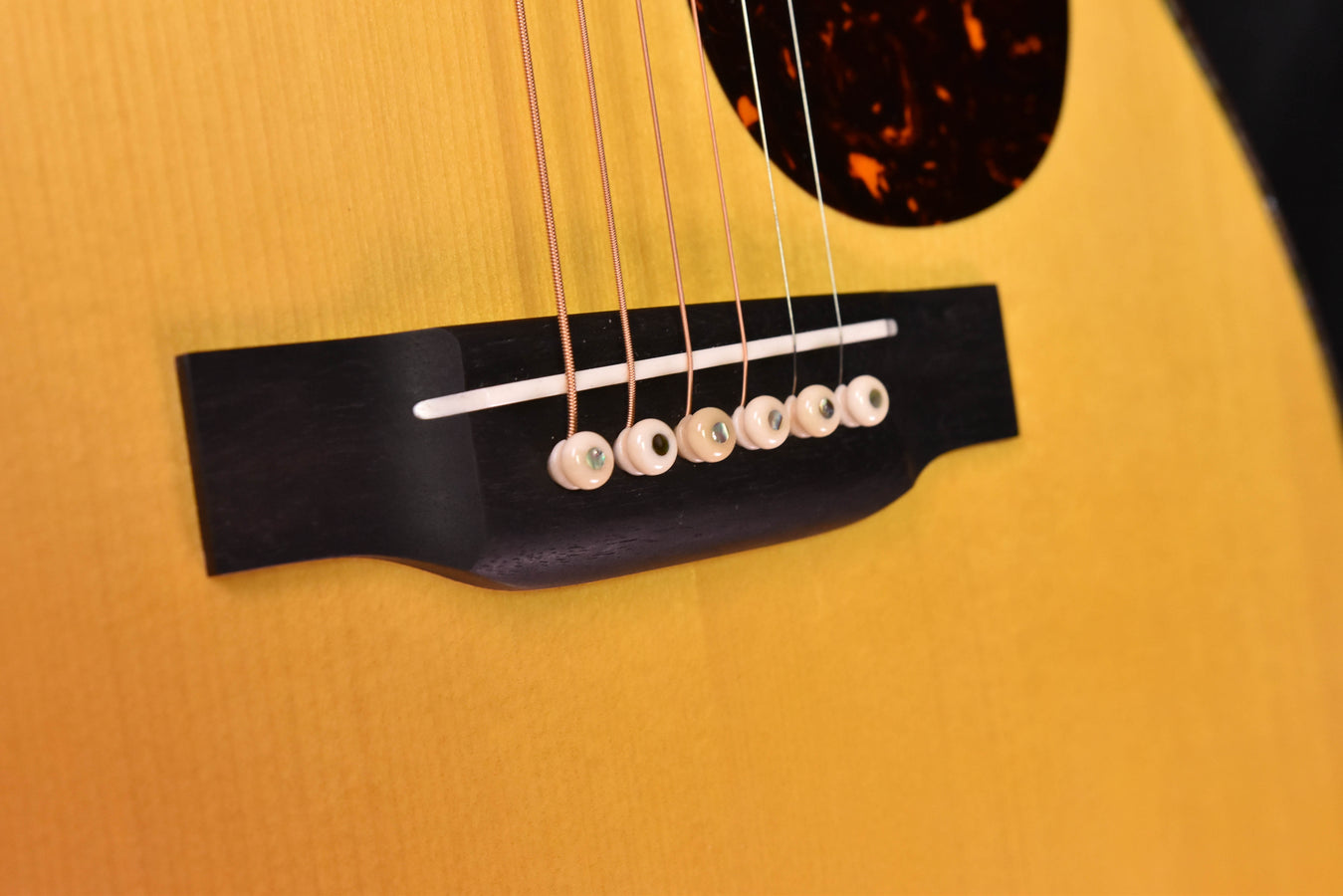 Acoustic guitar bridge and strings with white pins on a dark rectangular bridge plate