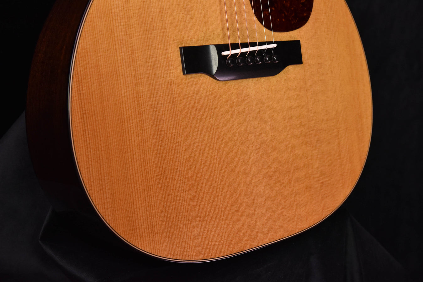 Acoustic guitar lower bout with black bridge and strings, natural wood finish.