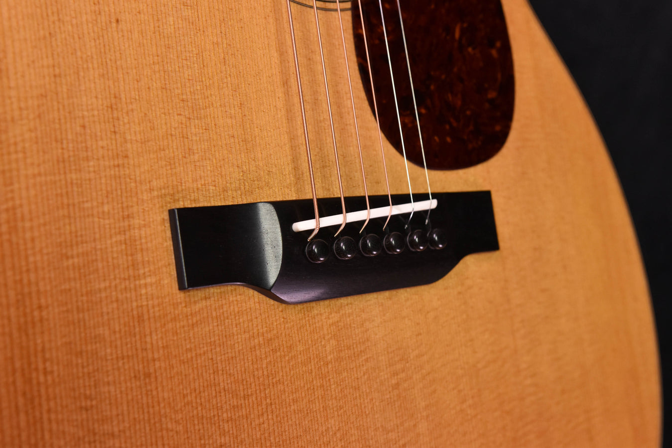 Close-up of black bridge and saddle with strings on natural acoustic guitar top.