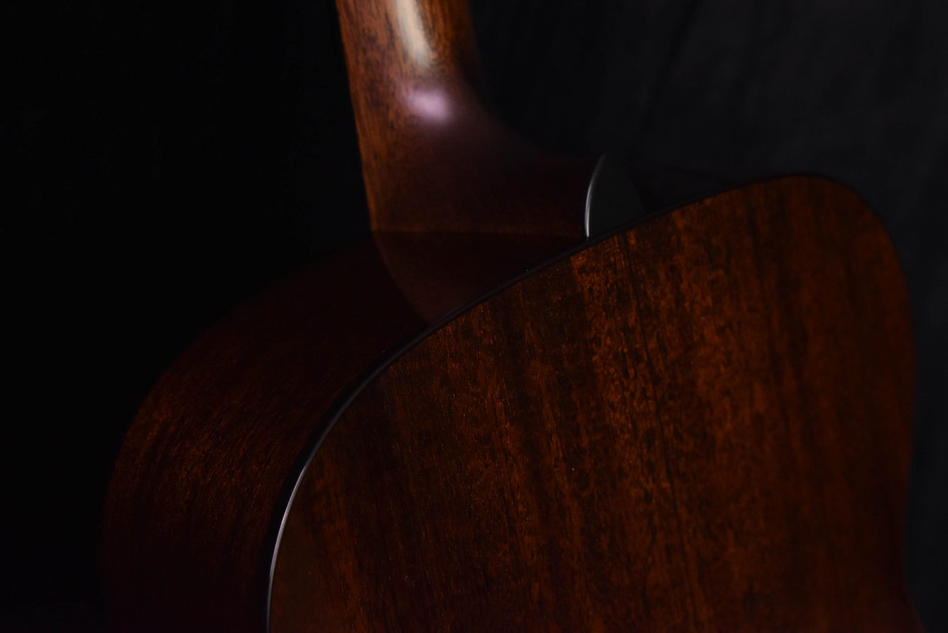 Acoustic guitar side profile showing curved dark wood body grain.
