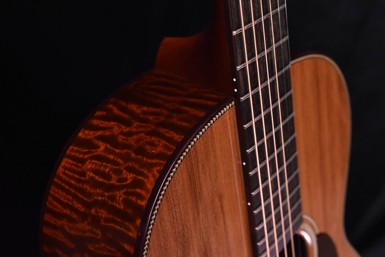 Quilted wood side and neck joint with bound edge, fretboard strings visible