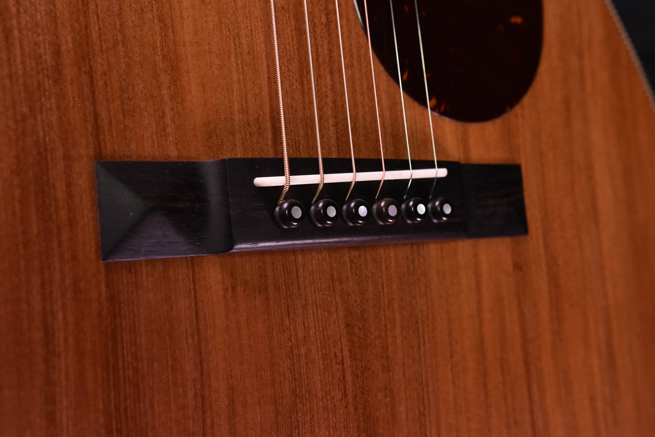 Bridge area of acoustic guitar with black bridge plate and metal saddle, strings visible
