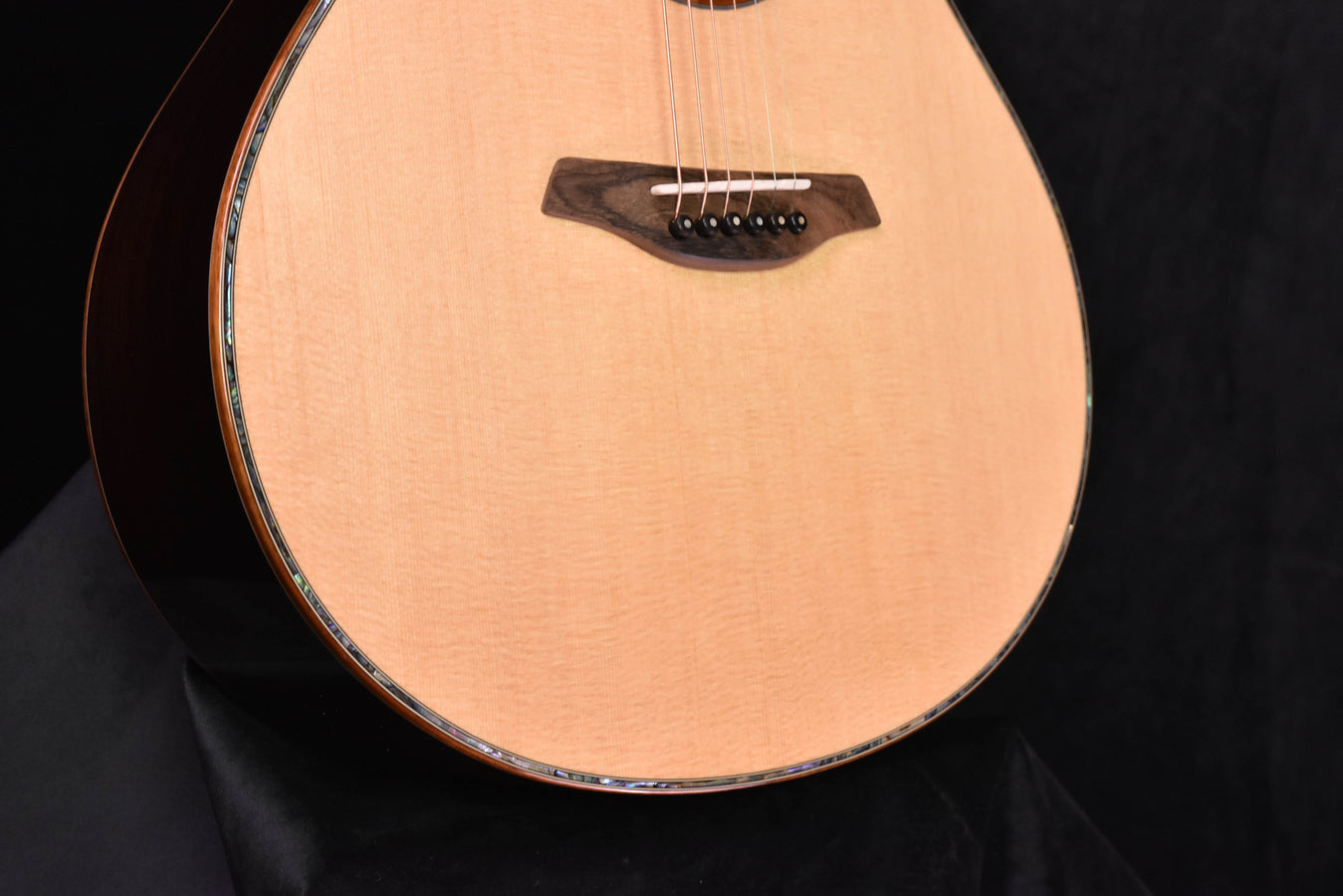 Acoustic cutaway guitar body close-up with bridge, strings, and dark pickguard-style plate