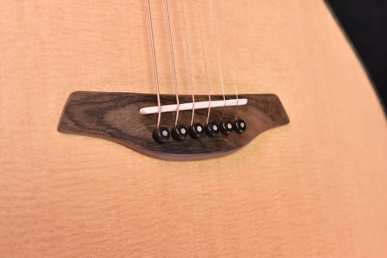 Bridge close-up on acoustic cutaway guitar: saddle, strings, and dark bridge cover