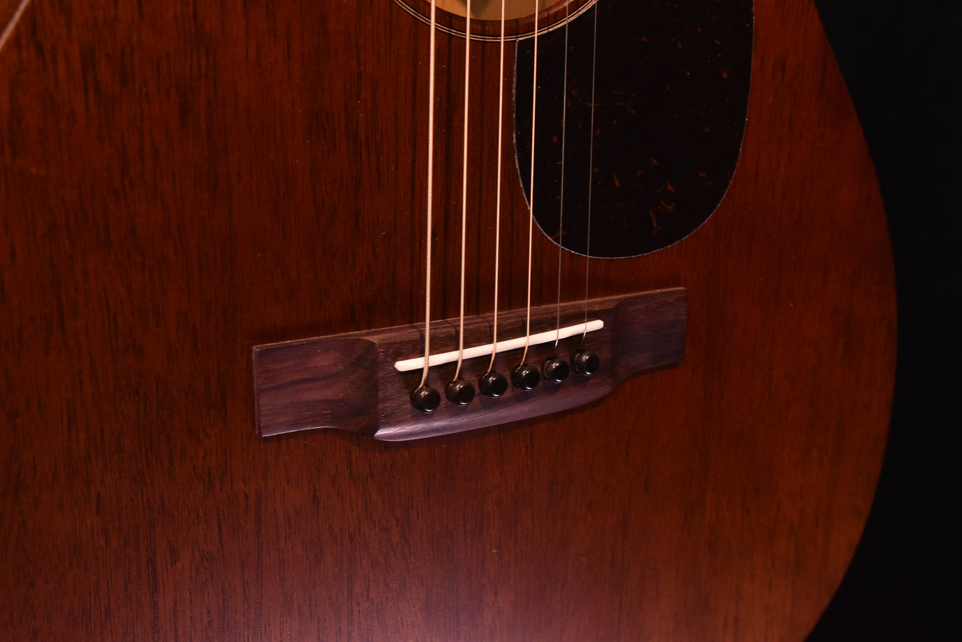 Mahogany acoustic guitar bridge with six strings and trapezoid bridge plate
