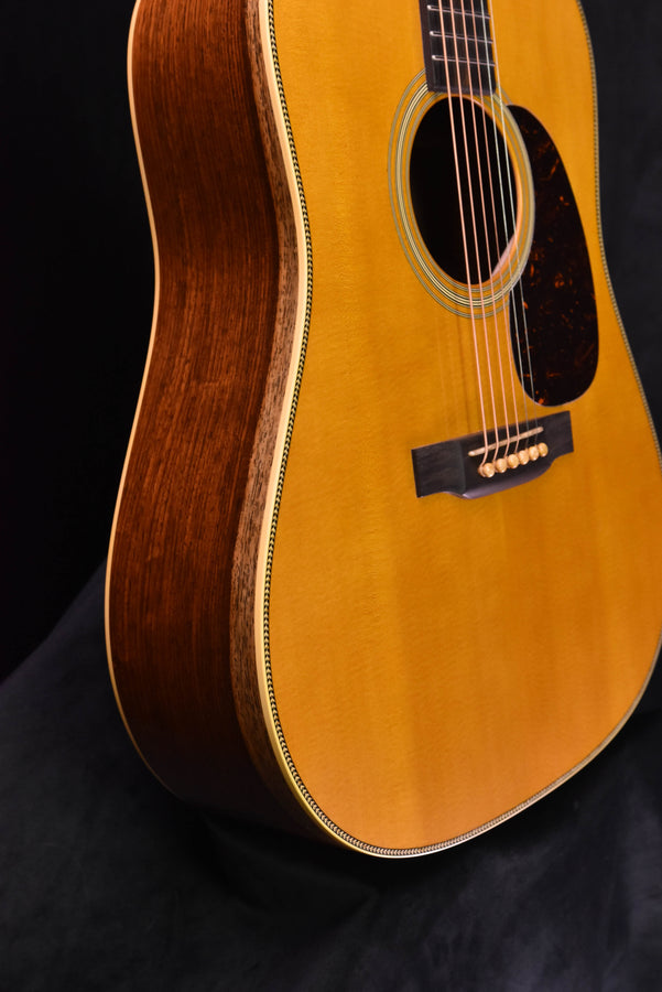Side profile of natural dreadnought acoustic guitar with dark wooden back and binding