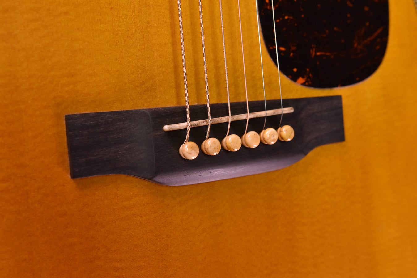 Close-up of dreadnought acoustic guitar bridge with six saddle pins and strings