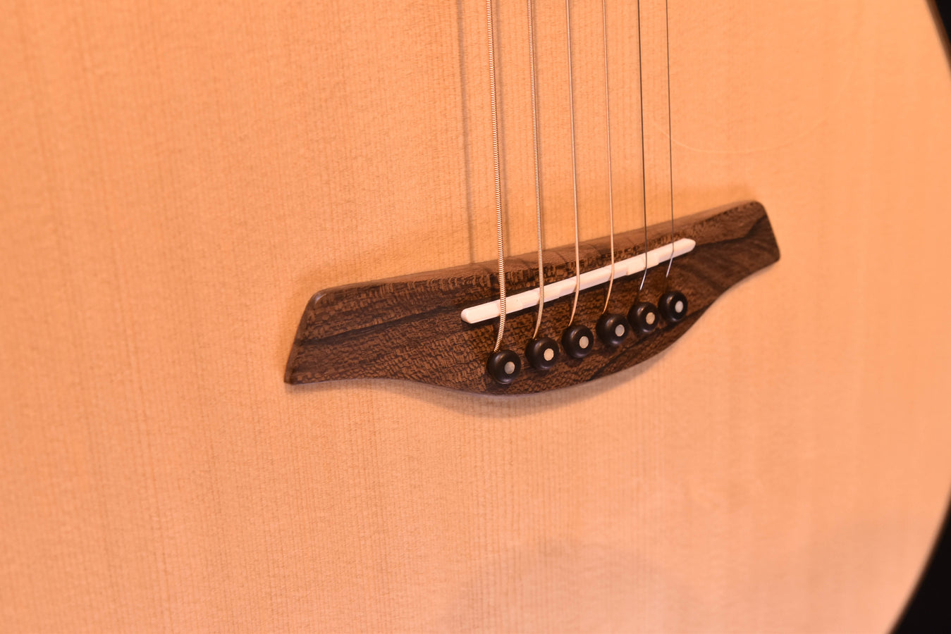 Used acoustic guitar bridge with dark saddle and six metal tuning pins at the headstock