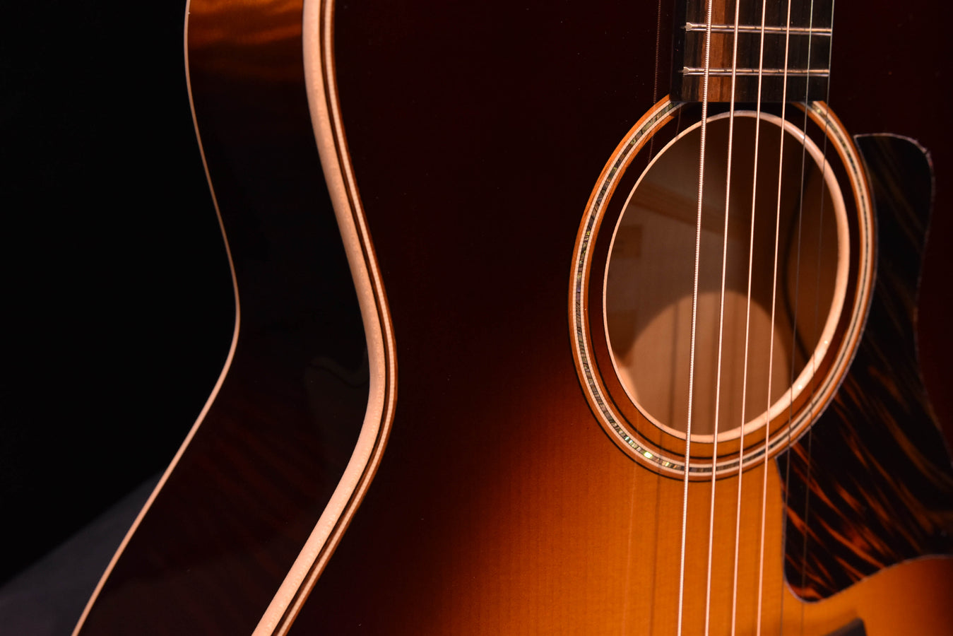 Close-up of soundhole and dark pickguard on tobacco sunburst acoustic guitar