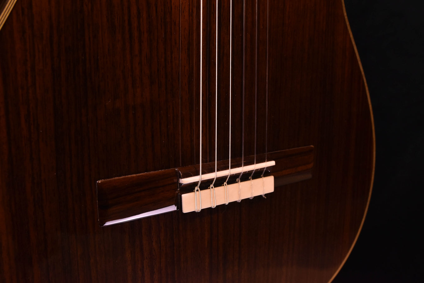 Bridge area with white saddle and strings on brown wooden guitar top