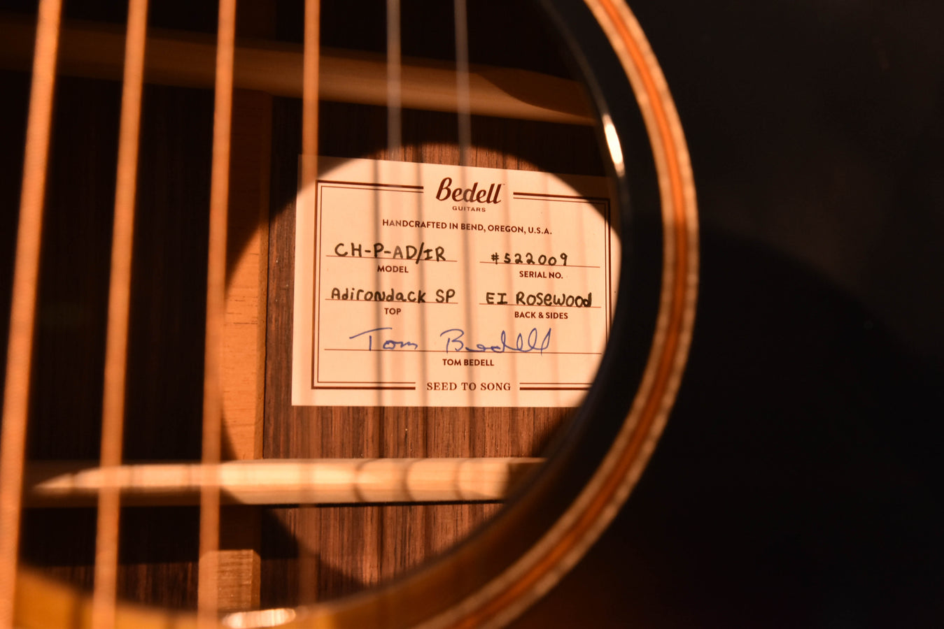 Acoustic guitar label on wood back near strings, “Bedell” visible